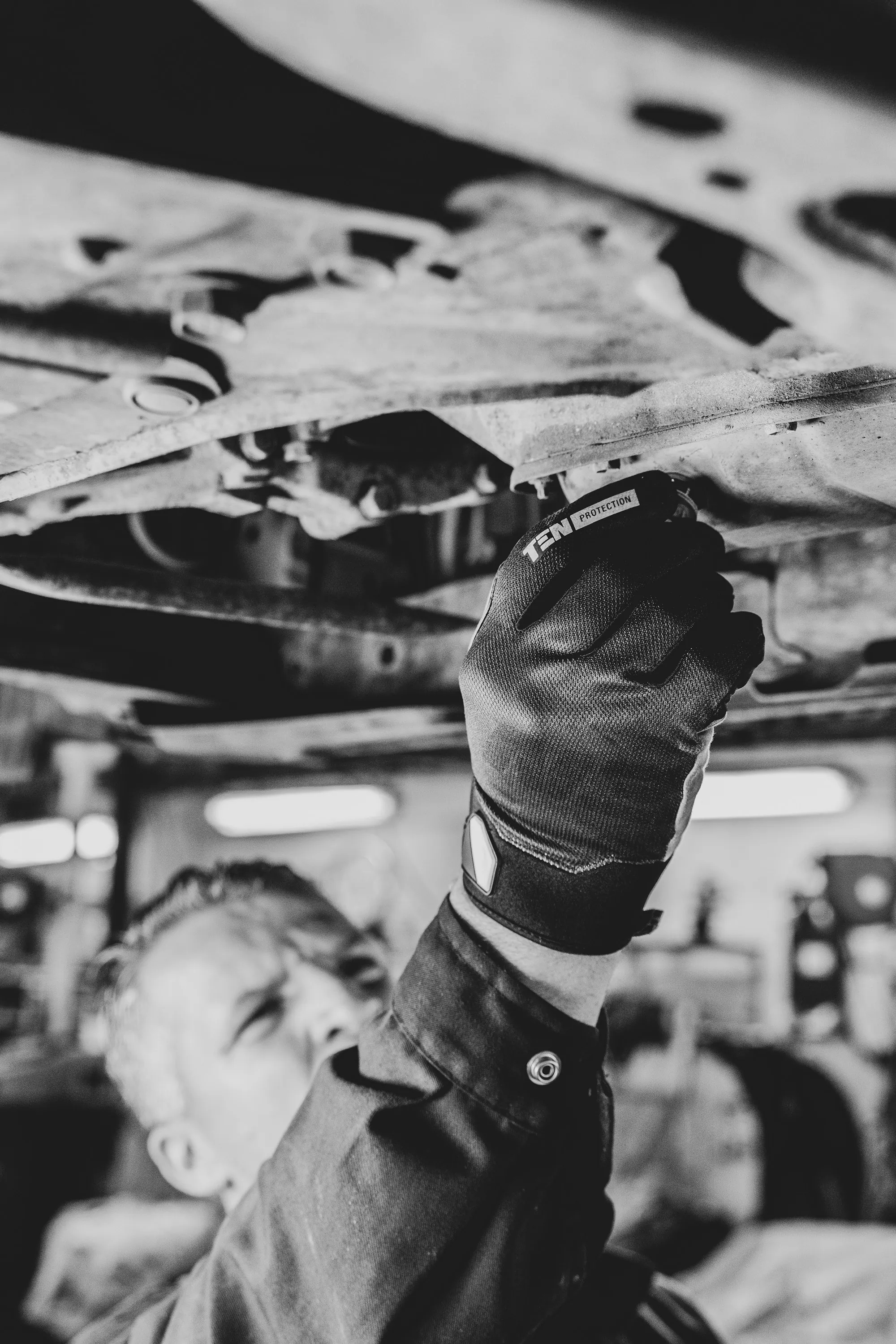 Black and white photo of a mechanic working under a vehicle