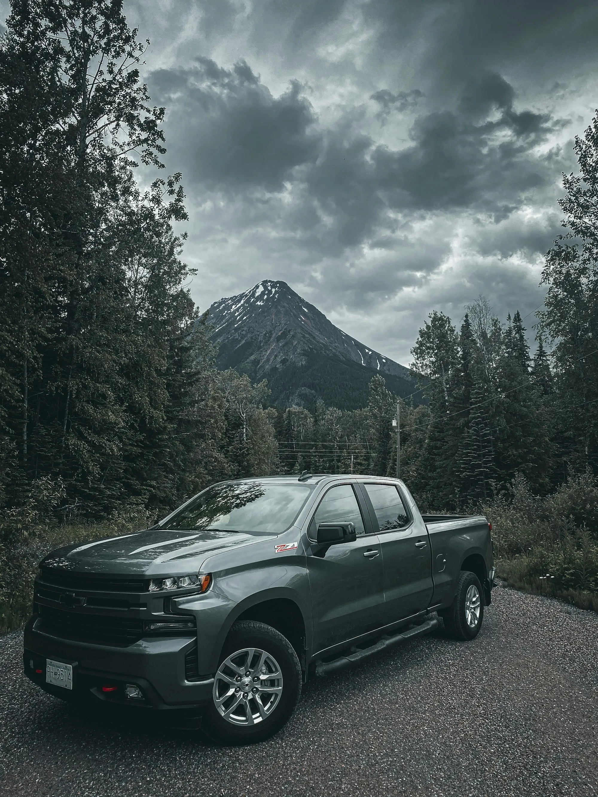 Dark pickup on a forest road below a mountain peak
