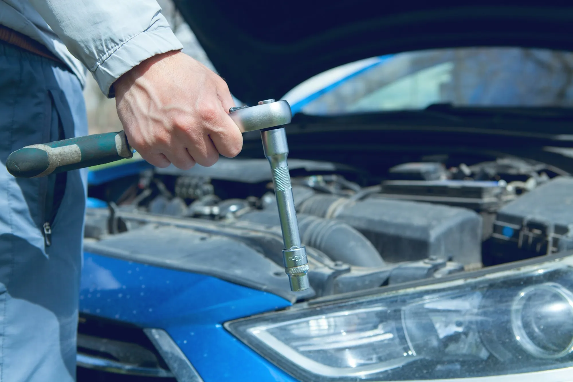 Hand turning a ratchet on an engine beside a blue car