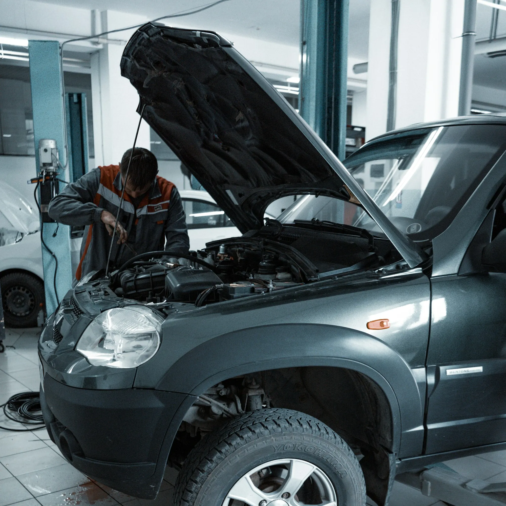 Mechanic working inside the engine bay of a grey SUV